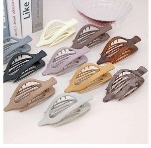 Multiple colors of hollow leaf oval hair clips displayed on a minimalist desk surface