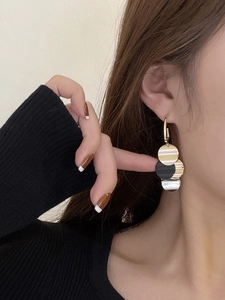 Close-up of long tassel earrings with metallic circles in gold, silver, and black on a model