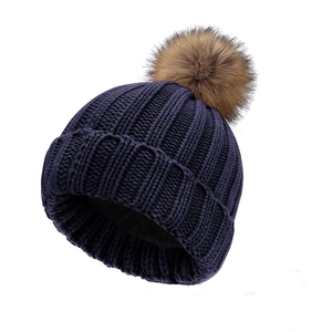 Detailed close-up of navy knit winter hat with thick texture and brown faux fur pompom