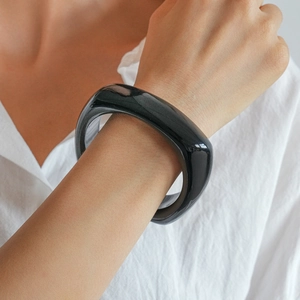 Close-up of a minimalist glossy black acrylic geometric square bangle on a wrist