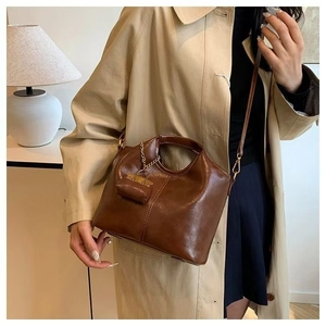 Brown vintage oil wax leather tote bag with charm accessory styled on a beige trench coat