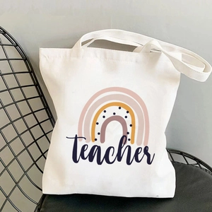 Detail view of white canvas tote bag with rainbow print and teacher text on a chair