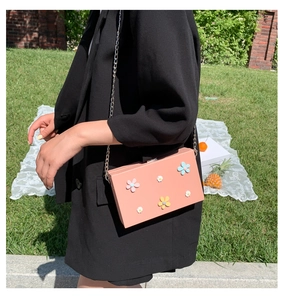 Pink chain bag with 3D floral accents shown outdoors in a stylish lifestyle setting