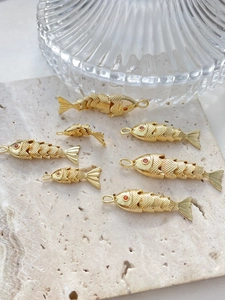 Detailaufnahme von 14k vergoldeten Fisch-Anhängern mit roten Augen auf Steinfliese