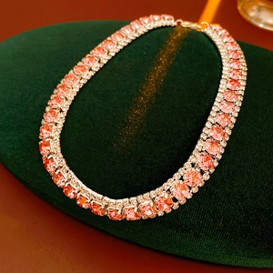 Detailed view of a pink crystal necklace on dark green velvet background with side accents