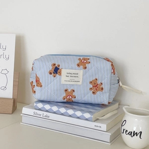 Quilted cotton makeup bag with blue stripes and bear prints on books in a cozy setting