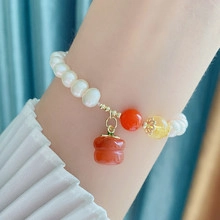 Detailed close-up of a pearl bracelet with red bell charm on a model wrist
