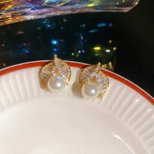 Gold leaf stud earrings with sparkling cubic zirconia and a white pearl on a tray