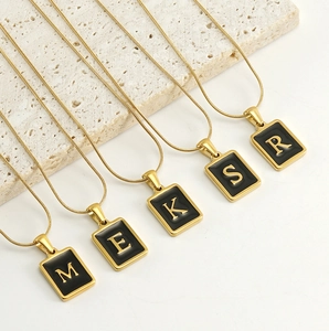 Détail de pendentifs carrés en acier doré 18k avec lettres en émail noir brillant