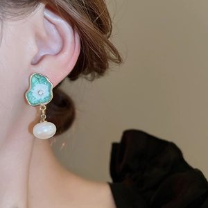 Gros plan sur les boucles d'oreilles lotus en émail vintage avec perle baroque et diamant