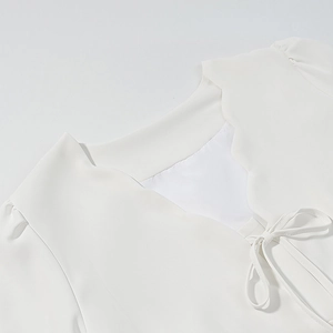 Détail du haut blanc présentant un col festonné élégant et un nœud décoratif à l'encolure