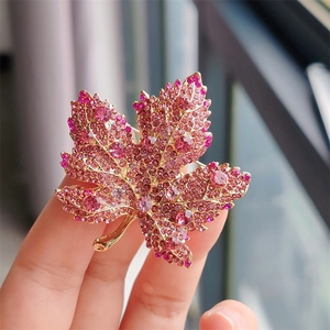 Detailed macro view of a luxury maple leaf brooch with pink crystals on golden metal