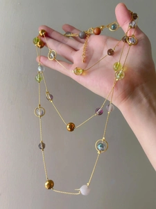 Close-up of a multi-colored stone beaded necklace with a golden chain held in hand