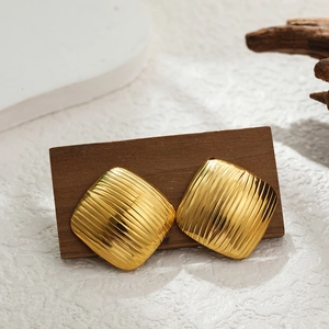 Detail of square gold hoop earrings with vertical stripes on a wooden stand
