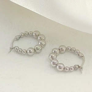 Macro shot of silver beaded hoop earrings with high-polish finish on white silk