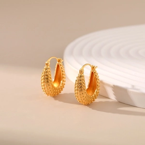 Close-up of golden horseshoe earrings with textured bead pattern and 18K gold plating
