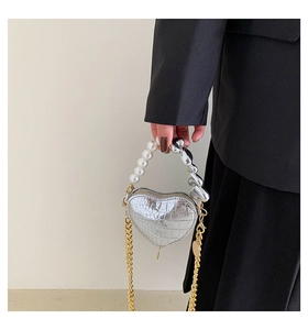 Détail du mini sac argenté en forme de cœur avec poignée en perles et texture crocodile