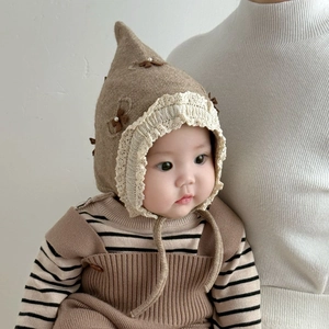 Detail of baby elf hat showing lace trim, brown bow with pearl and knit texture
