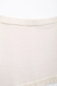 Detail of cream knit skirt featuring textured fabric and delicate fringe hemline decoration
