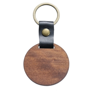 Detail of round walnut wood keychain with black leather strap and bronze metal ring