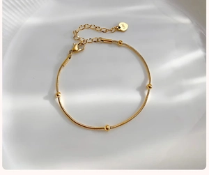 Close-up of golden bead bracelet with 18K heart tag on white textured plate