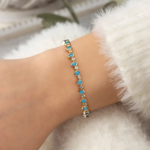 Close-up of golden bracelet with turquoise teardrop stones and sparkling crystals on wrist