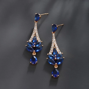 Detail of luxury gold earrings featuring pear-shaped blue zircons and white crystals