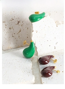Artistic detail of teardrop resin earrings in green and brown on white stone