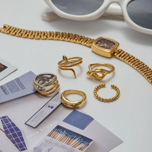 Flachbild von goldenen Schlangenringen und Vintage-Uhr mit modischen Accessoires gestylt