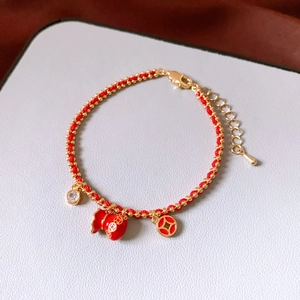 Detail of red braided bracelet with 18k gold-plated fortune bag and zircon charms