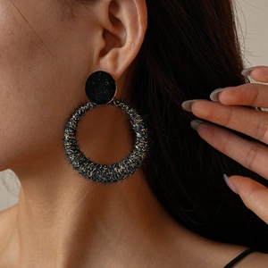 Detail view of round hollow wool earring in black with golden shimmer on model