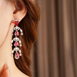 Detail of silver drop earrings featuring red heart gems and layered zircon tassels