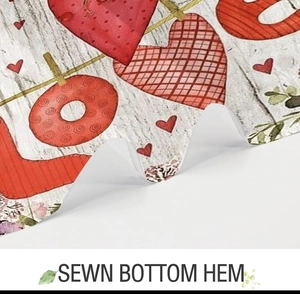 Detail showing the sewn bottom hem of the white fabric shower curtain with red love prints