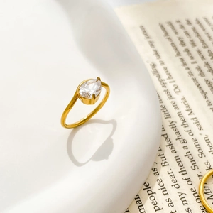 Detailed close-up of a pear-shaped zircon gold ring on a ceramic edge with vintage book