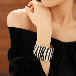 Close-up of a wide zebra print bangle with silver metal edges on a model wrist