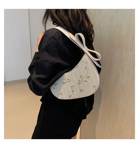 Detail of cream straw bag with green floral embroidery and large bow on strap