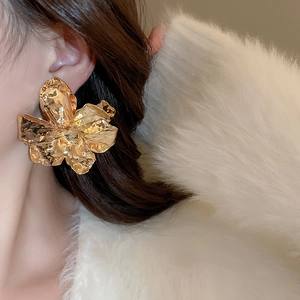 Detailed view of large gold metallic flower earrings with textured pleated petals on model