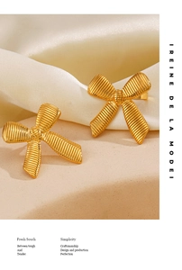 Detailed close-up of 18K gold-plated bow earrings with pleated texture on silk and sandstone
