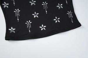 Détail de l'ourlet en maille côtelée noire avec fleur en strass argentés et franges