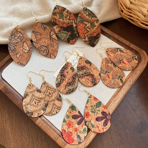 Close-up of bohemian teardrop earrings with floral leaf prints on cork in a wooden tray