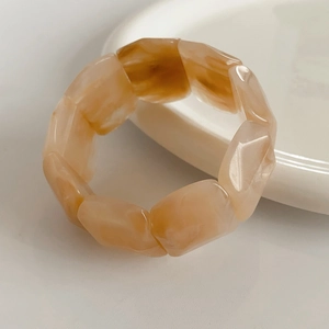 Detail of coffee marble acrylic wide stretch bracelet with natural stone texture on white plate