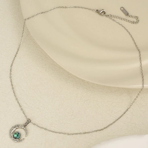 Detail of crescent moon necklace with green shell inlay on a white ceramic tray