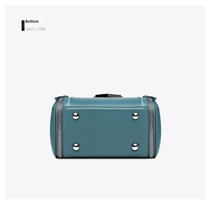 Detail view of teal handbag base featuring four silver protective metal feet and side zippers
