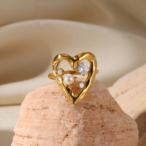 Detail shot of a gold heart ring with pearl and zircon inlay on a textured stone base