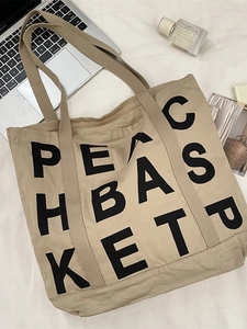 Khaki canvas tote bag with black letter print and wide straps in a lifestyle setting