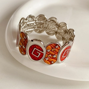 Détail macro du bracelet élastique vintage avec logo G en émail rouge et étoiles orange