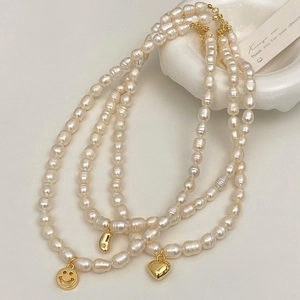 Close-up of Baroque pearl necklaces with gold smiley, heart, and pod pendants