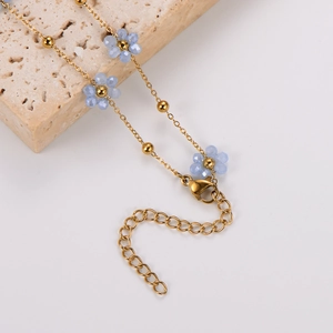 Detail of golden beaded necklace with blue crystal flowers and lobster clasp on stone