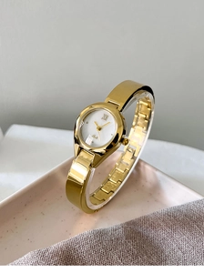 Detail view of a gold bangle watch with a white Roman numeral dial on a decorative plate