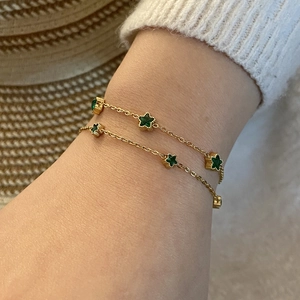 Bracelet vintage en acier doré avec breloques étoiles émeraude porté au poignet femme